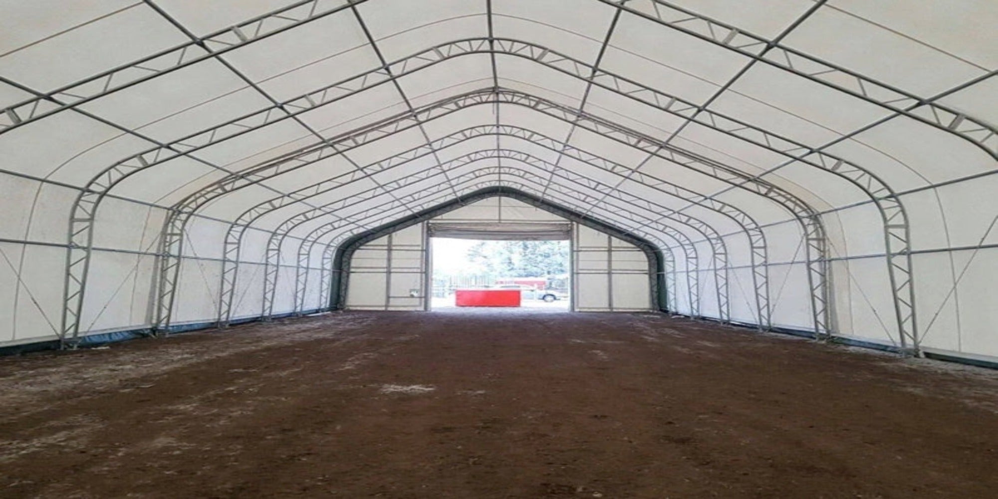 Interior view of a large, fabric-covered building with a metal frame and dirt floor.