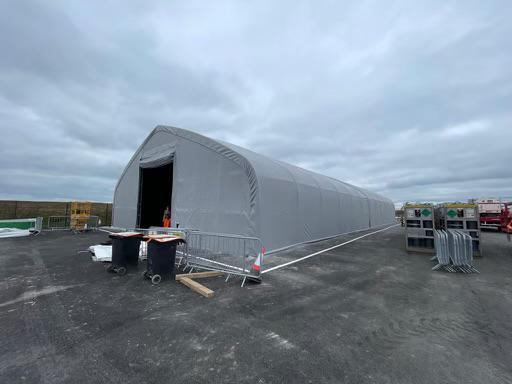 A gray Quonset hut style tent on an asphalt surface.