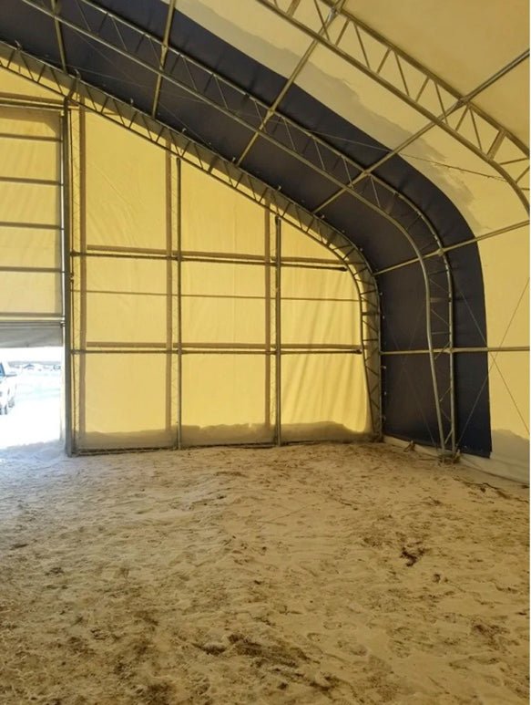 Interior of a large, metal-framed tent with tan fabric walls and a sand-covered floor.