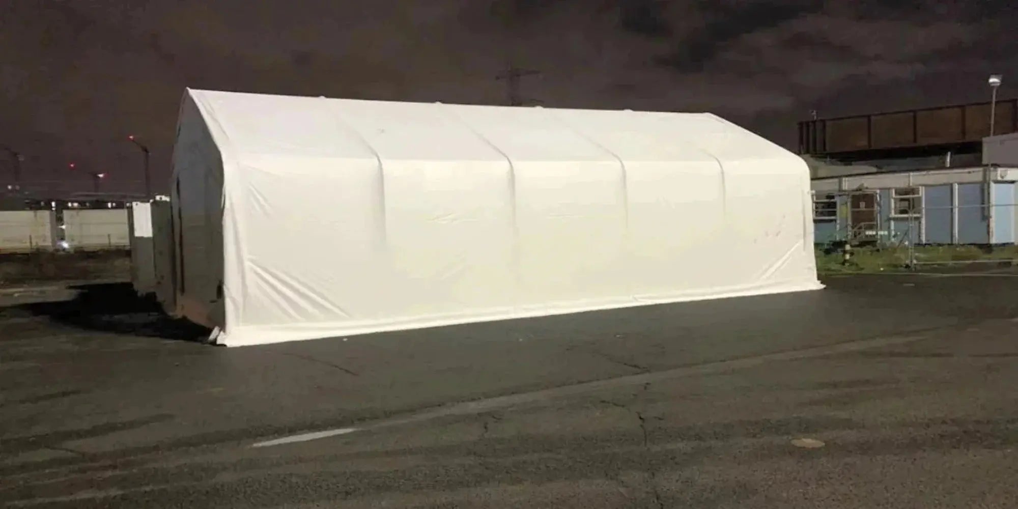 A large white tent stands on a dark paved surface outdoors at night.